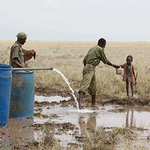 肯亞圖爾卡納郡大規模地下水調查定位計畫完成後，一位預備警察在地下水鑿孔送水給孩子。（攝影：Unesco。）